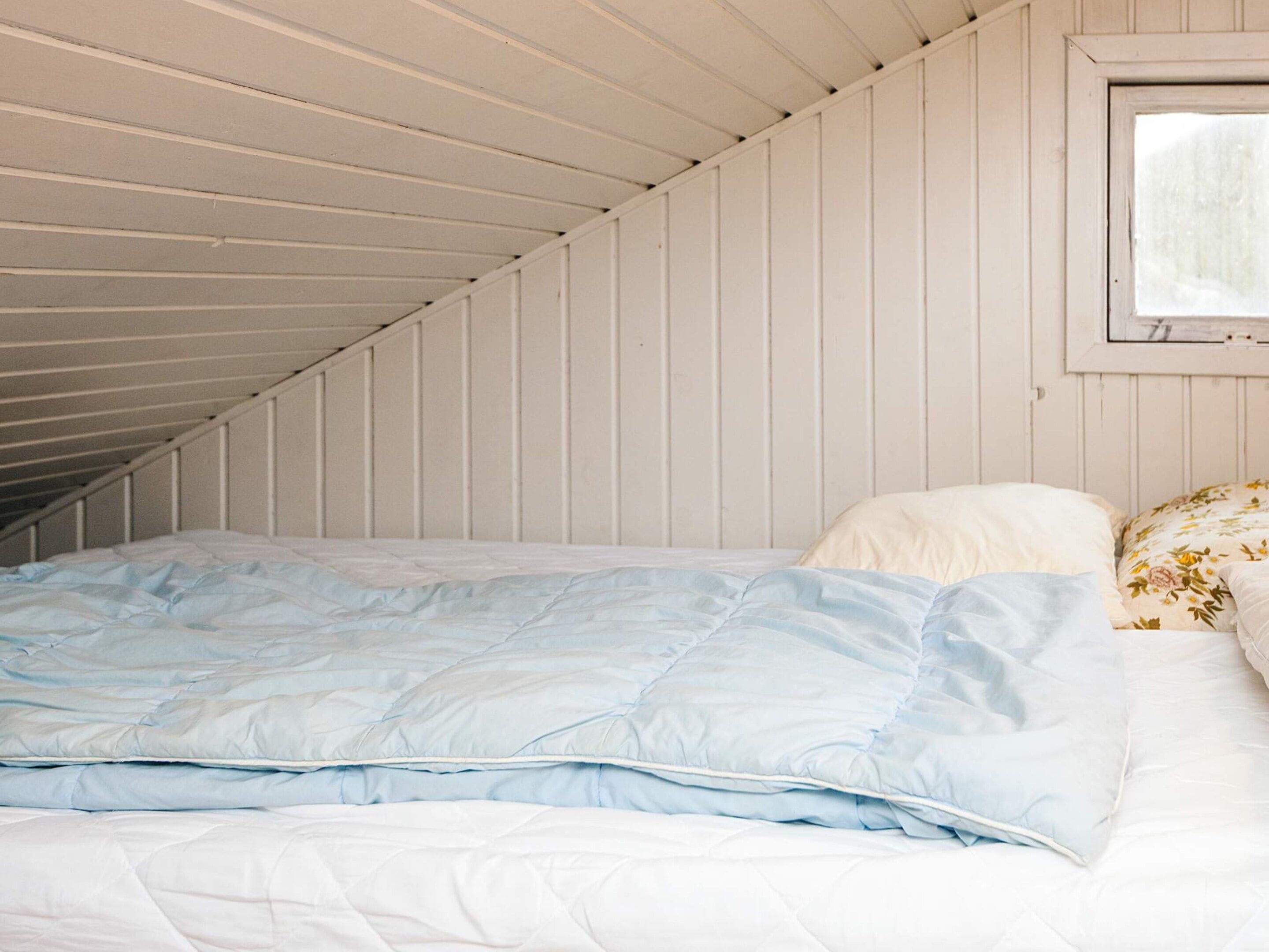 A bedroom with a sloped ceiling, a bed with a blue and white duvet, and a window with a view.