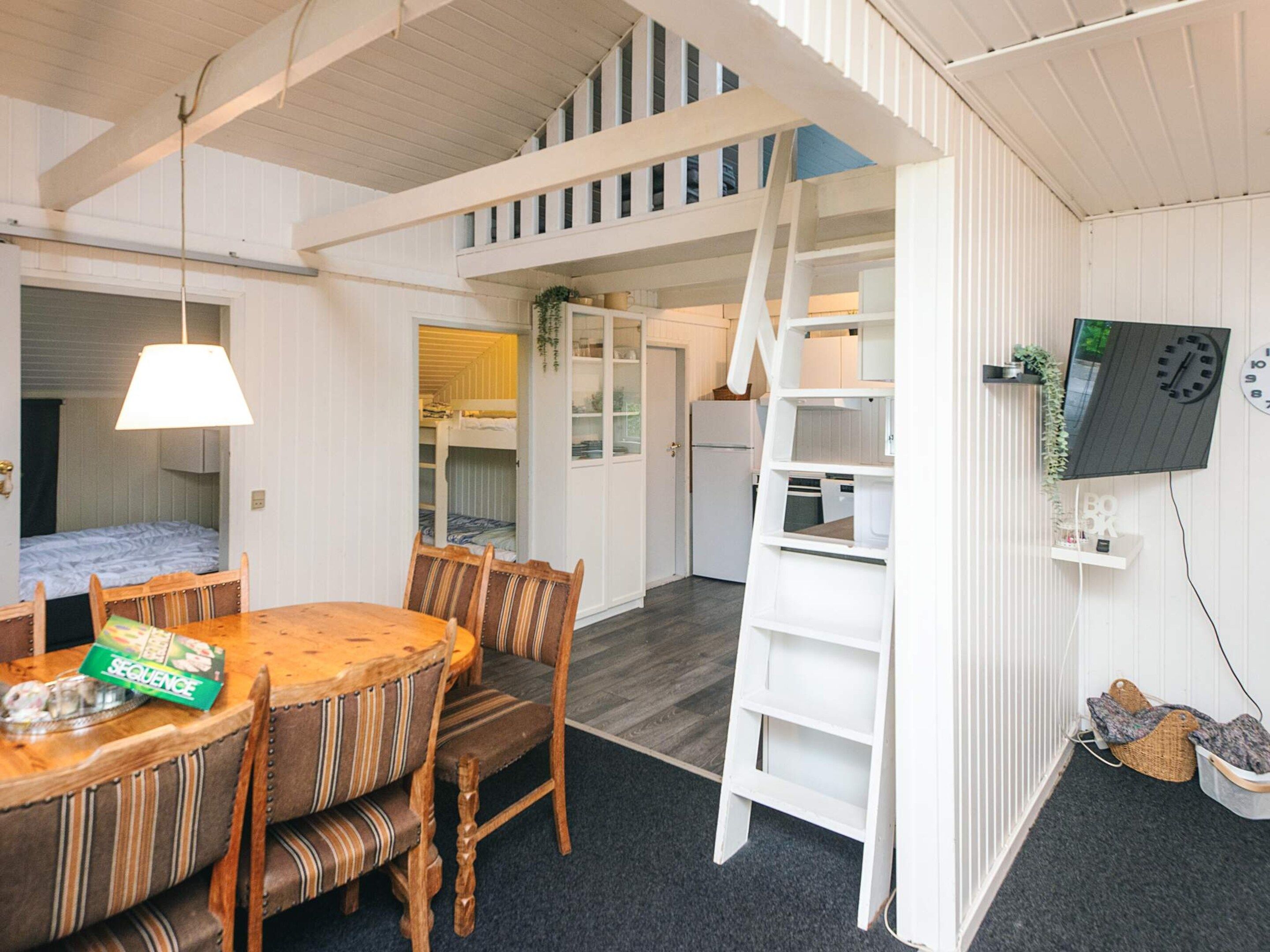 A compact room with a dining table, chairs, a ladder, a TV, and a bunk bed.