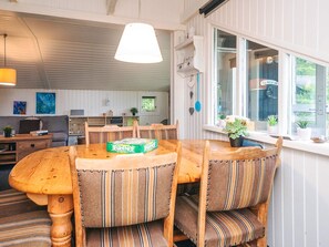 A cozy dining area with a wooden table and striped upholstered chairs, a hanging light fixture, and a window with a view of greenery. - 4 Person Holiday Home in Hemmet (Hemmet)