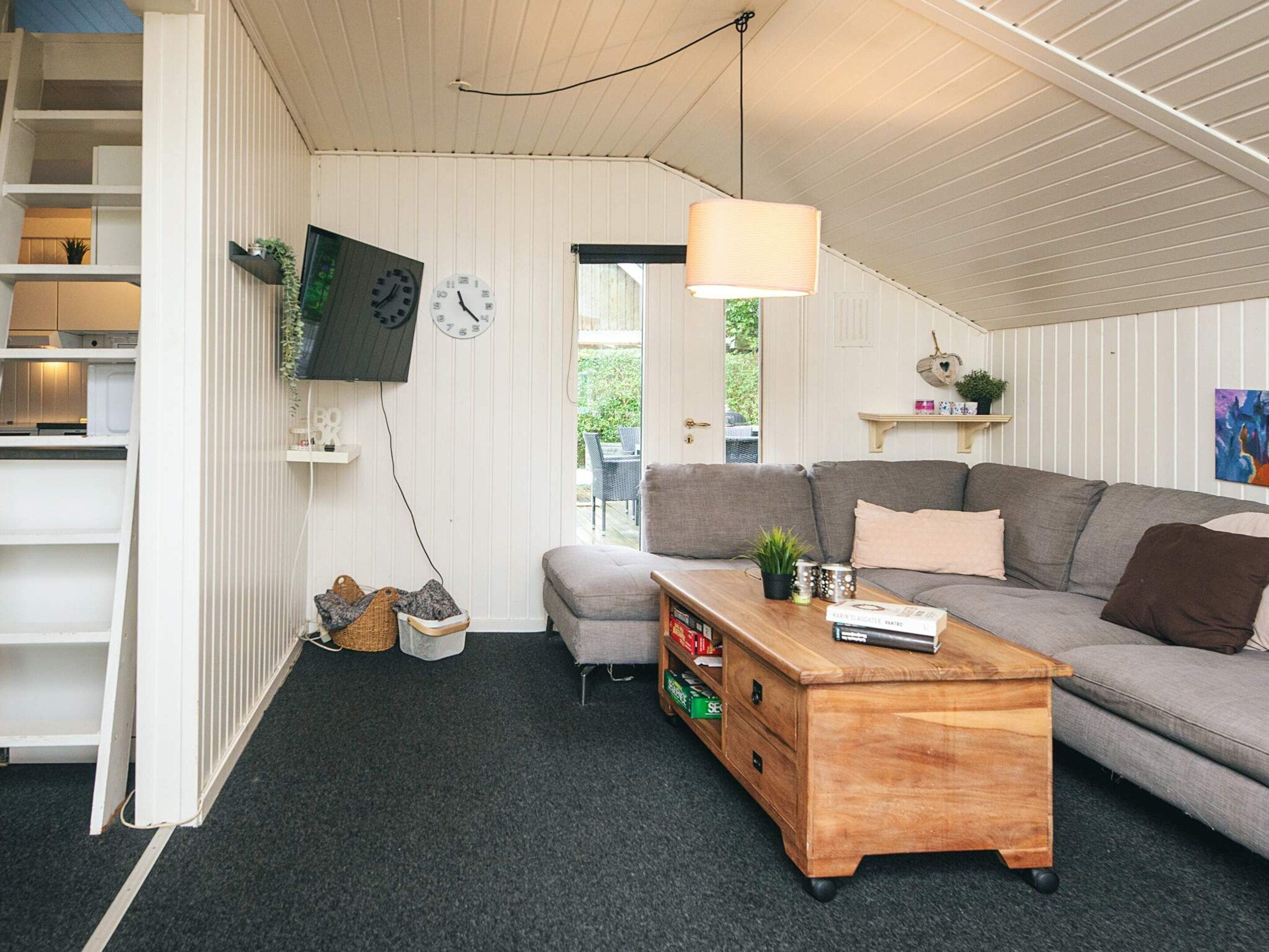 A cozy living room with a sofa, a wooden coffee table, a television mounted on the wall, and a ceiling fan.