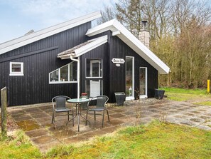 En svart byggnad med ett vitt tak, en skorsten och en skylt med texten ”Damm-Ida”. Utanför finns det två stolar och ett bord.