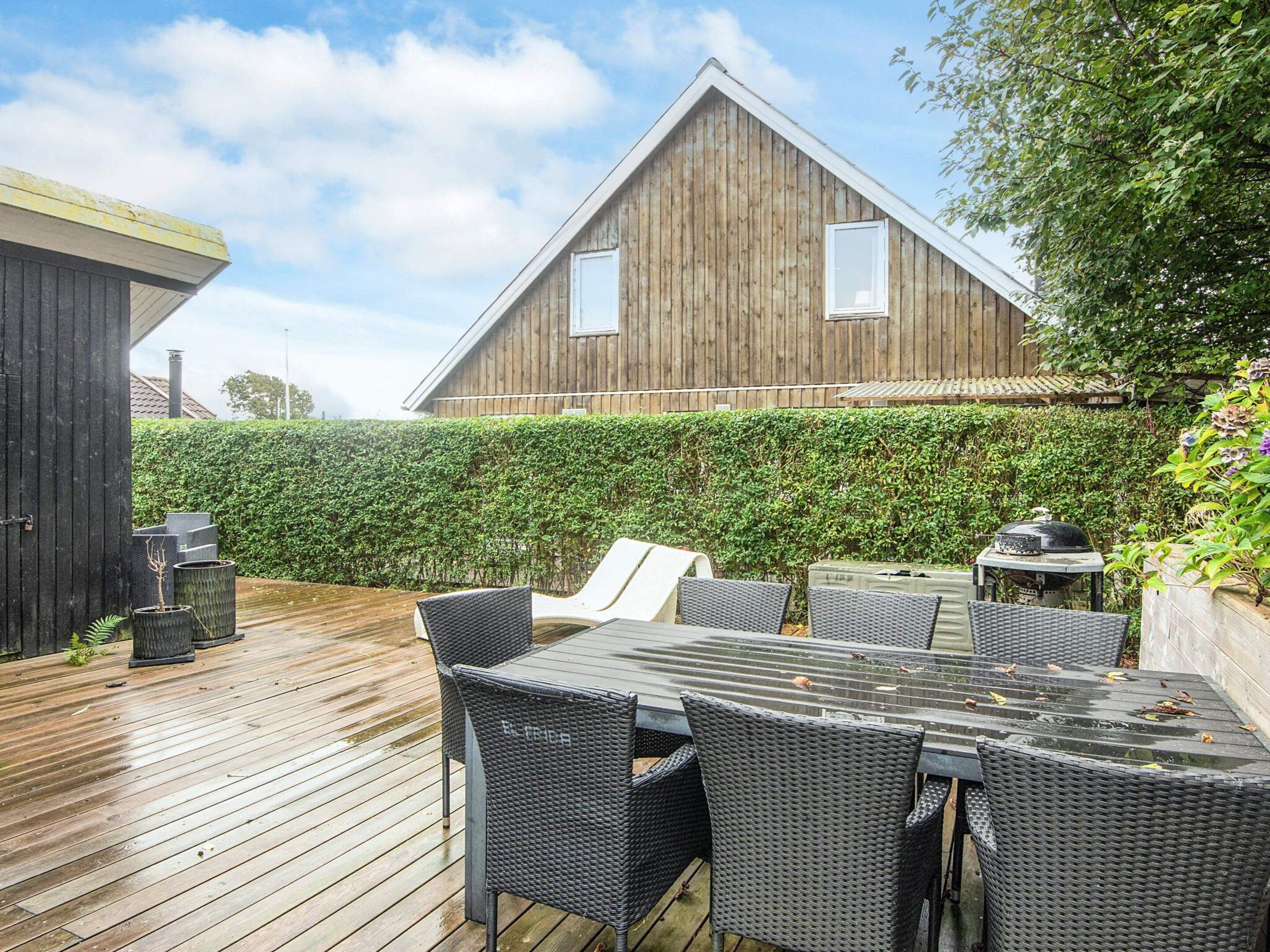 A wooden deck with outdoor furniture, a hedge, and a large barn structure.