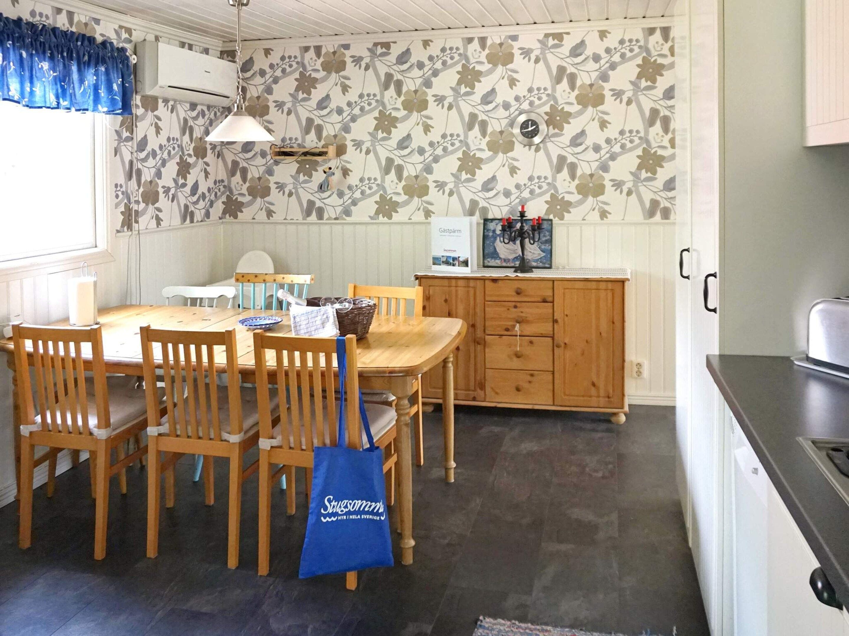 Un comedor con una mesa y sillas de madera, una bolsa de tela azul y una pared con papel tapiz floral.