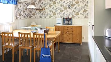 A dining area with a wooden table and chairs, a blue tote bag, a clock on the wall, and a cabinet with a candle holder.