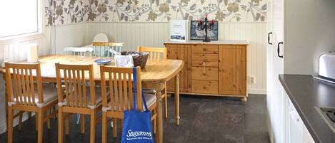 A dining area with a wooden table and chairs, a blue tote bag, a clock on the wall, and a cabinet with a candle holder.