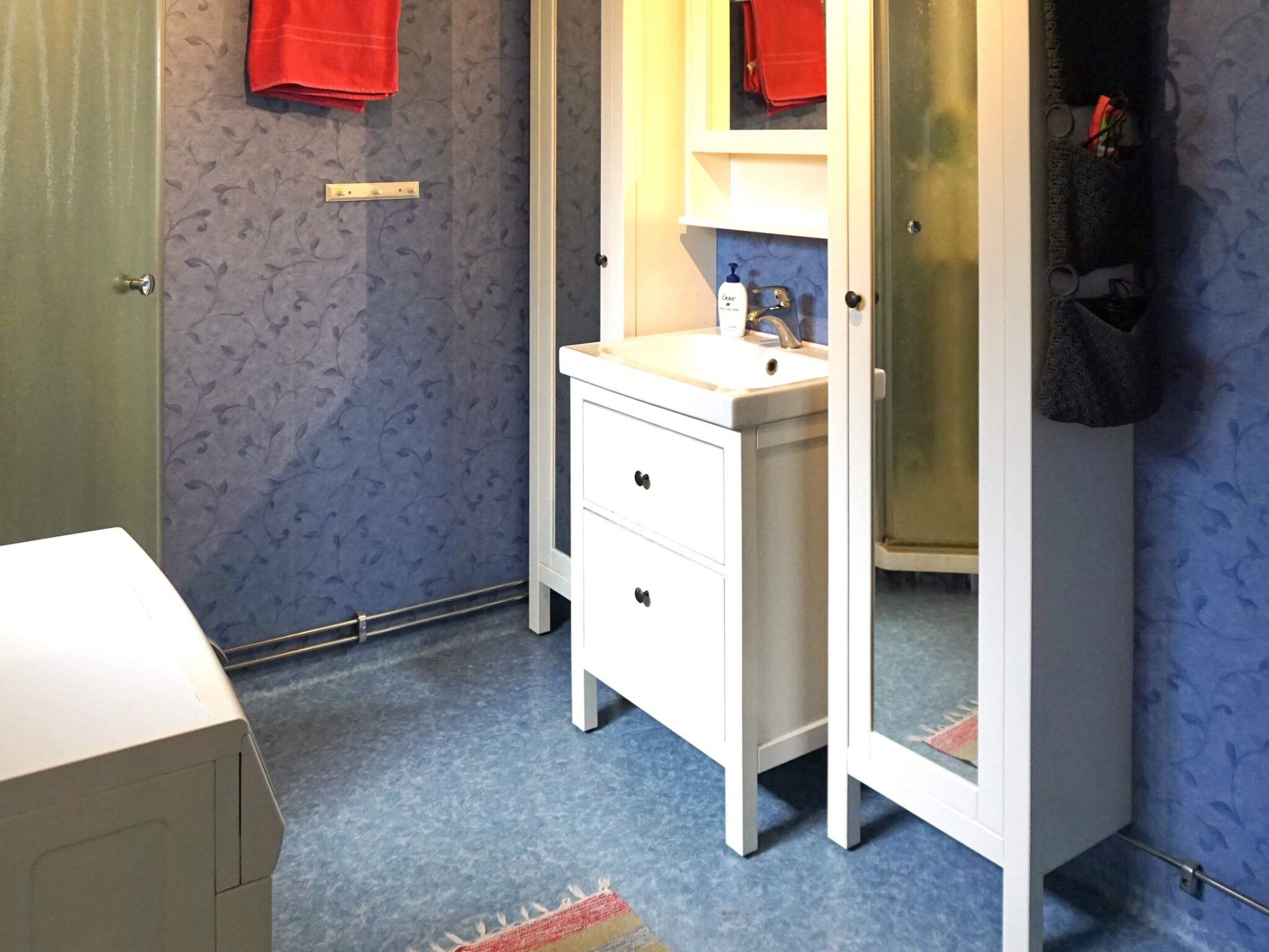 A bathroom with a white vanity, a mirror, a towel rack, and a shower area.