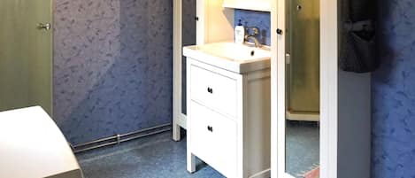 A bathroom with a white vanity, a mirror, a towel rack, and a shower area.