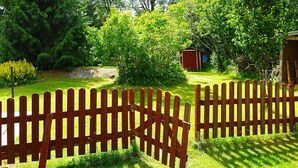 Une clôture en bois dans un jardin, avec un petit abri de jardin et un feuillage dense en arrière-plan.