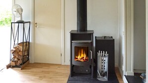 Une pièce avec un poêle à bois, une porte, un ventilateur et une pile de bois de chauffage.