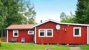 Une maison en bois rouge avec un toit rouge, une antenne parabolique et un banc à l’extérieur.
