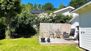 En baghave med træterrasse, udendørs møbler og et hegn.