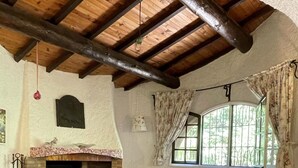 Ein gemütliches Zimmer mit Steinfußboden, Kamin, einer Couch und einem Fenster mit Vorhängen.