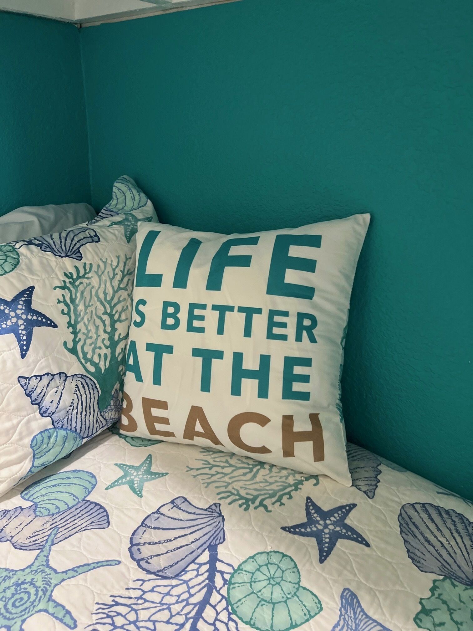 Ein Bett mit türkisfarbenen Wänden und einem Kopfkissen mit Strandmotiv.