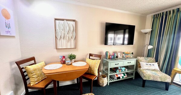 Una habitación acogedora con una mesa de madera para comer, sillas, un televisor y una cama con cortina a rayas.
