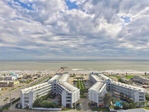 Un hôtel en bord de mer, à l’architecture symétrique, doté de plusieurs étages et de balcons, situé près d’une plage offrant une vue dégagée sur l’océan.