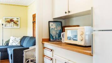 A compact living space with a kitchenette, a sofa, a wicker chair, and a framed picture on the wall.