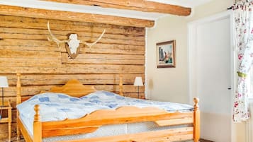 A wooden bed with a headboard, a wall-mounted animal skull, a framed picture, and a door with floral curtains.
