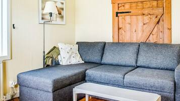 A living room with a grey sectional sofa, a white side table, a floor lamp, and a wooden wall panel.