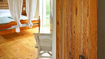 A wooden room with a bed, a wicker chair, and a wooden door.
