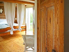 Une pièce en bois avec un lit, des rideaux et une chaise en osier.