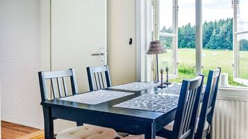 A dining area with a table and chairs, a window with a view of a green landscape, and a lamp on the table.