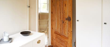 A room with a white dresser, a wooden door, and a wicker chair.