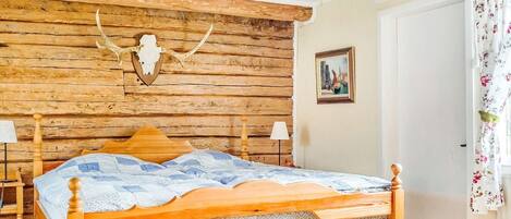 A wooden bed with a headboard, a wall-mounted animal skull, and a framed picture on the wall.