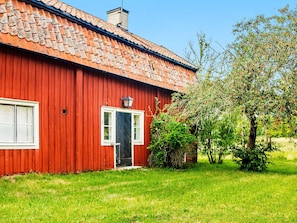 Una casa de madera roja con techo de tejas, una puerta principal y un pequeño porche.