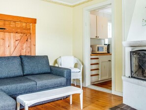A living room with a grey sofa, a white armchair, and a white coffee table. There is a wooden door and a white cabinet with a microwave on top.