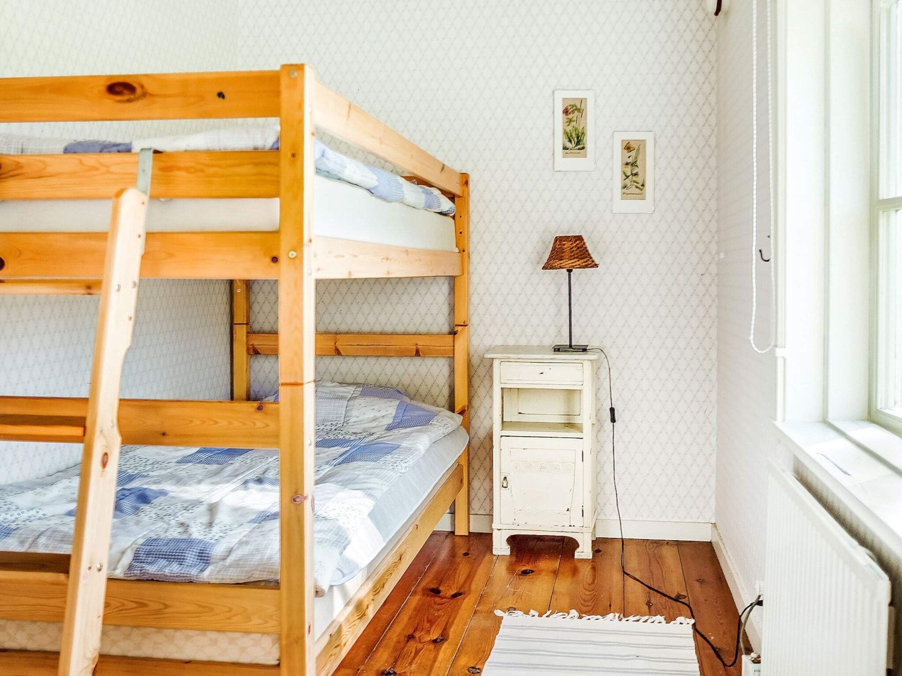 Una cama litera con una mesita de noche pequeña y una lámpara, un radiador y una ventana con vistas.