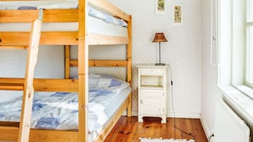 A bunk bed with a small bedside table and a lamp, a radiator, and a window with a view.
