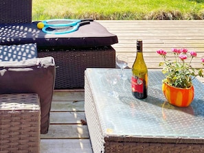 An outdoor seating area with wicker furniture, a glass table, a bottle of wine, and a vase with flowers. - 6 Person Holiday Home in Nexo (Akirkeby)