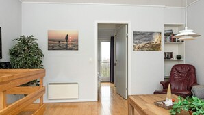 Ein modernes Wohnzimmer mit Holzboden, einem schwarz-weißen StreifenTeppich, einem roten Ledersessel, einem Holztisch und einem Bücherregal.