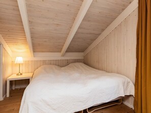 A bedroom with a wooden ceiling, a bed with a white bedspread, a bedside table with a lamp, and wooden walls.