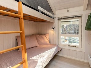 A bunk bed with a ladder, a window with a view of trees, and a wall-mounted light fixture.