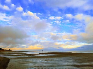 A beach with wide sandy areas and a distant view of the sea under a partly cloudy sky.