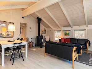 A cozy living room with a high ceiling, a fireplace, a dining area with chairs, and a sofa.