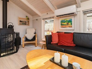 A cozy living room with a fireplace, a black leather sofa, a wooden chair, and a table with candles.
