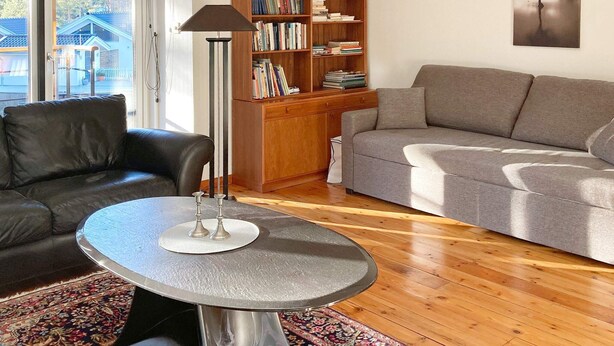 Un salon avec un canapé en cuir, un canapé gris, une bibliothèque en bois et une table ronde sur laquelle se trouve une lampe.