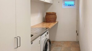 Une buanderie équipée d’un lave-linge, d’une étagère avec un panier, et d’une petite fenêtre donnant sur l’extérieur.