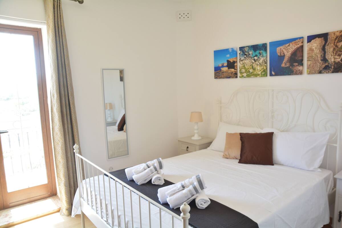 A hotel room with a bed, a nightstand, a mirror, and a window with curtains.