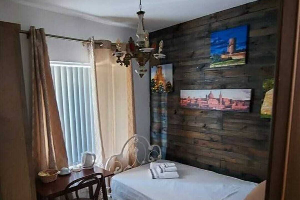 A bedroom with a bed, a desk, and a chair. There is a wooden wall with pictures and a ceiling fan.