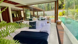A modern bedroom with a large bed, a glass-enclosed patio, a dining area, and a swimming pool. - House with beautiful pool and private cook! (Mata de São João)
