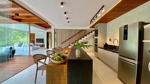 A modern kitchen with a central island, stainless steel appliances, and a dining area with wicker chairs. - House with beautiful pool and private cook! (Mata de São João)