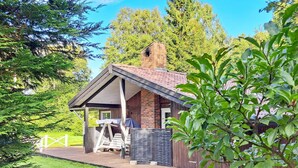 A wooden cabin with a sloped roof, a brick chimney, and a deck with outdoor furniture. - 5 Person Holiday Home in Frederiksvaerk (Frederiksvaerk)