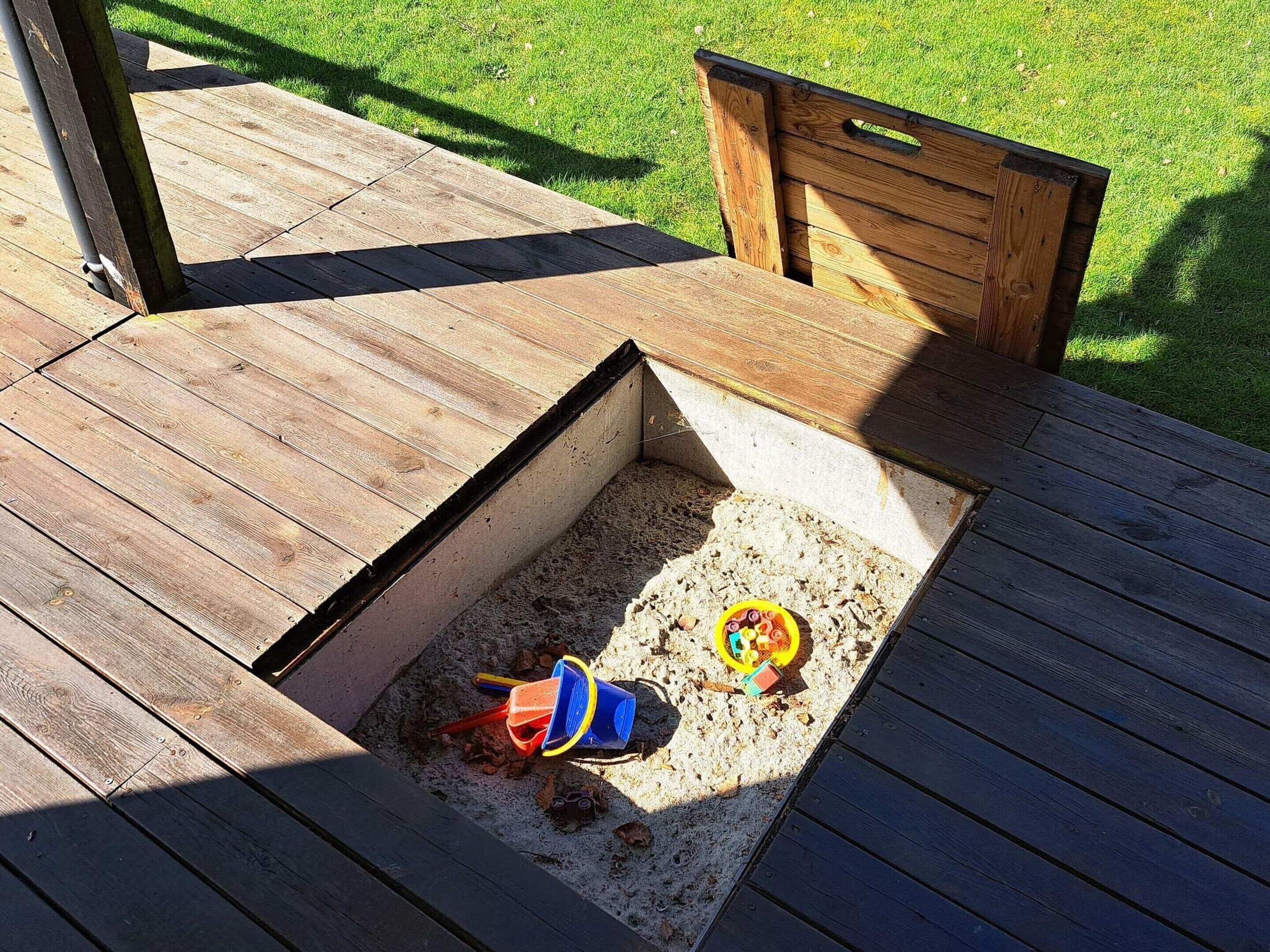 Una terraza de madera con un área de arenero que contiene juguetes y arena.