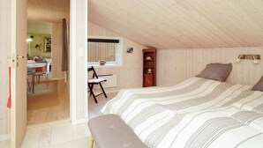 A cozy attic bedroom with a sloped ceiling, a bed with striped bedding, a small desk with a chair, and a wooden shelf with decorative items. - 5 Person Holiday Home in Frederiksvaerk (Frederiksvaerk)