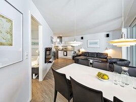 Et moderne køkken med hvide skabe, et spiseområde med et hvidt bord og en grå sofa.