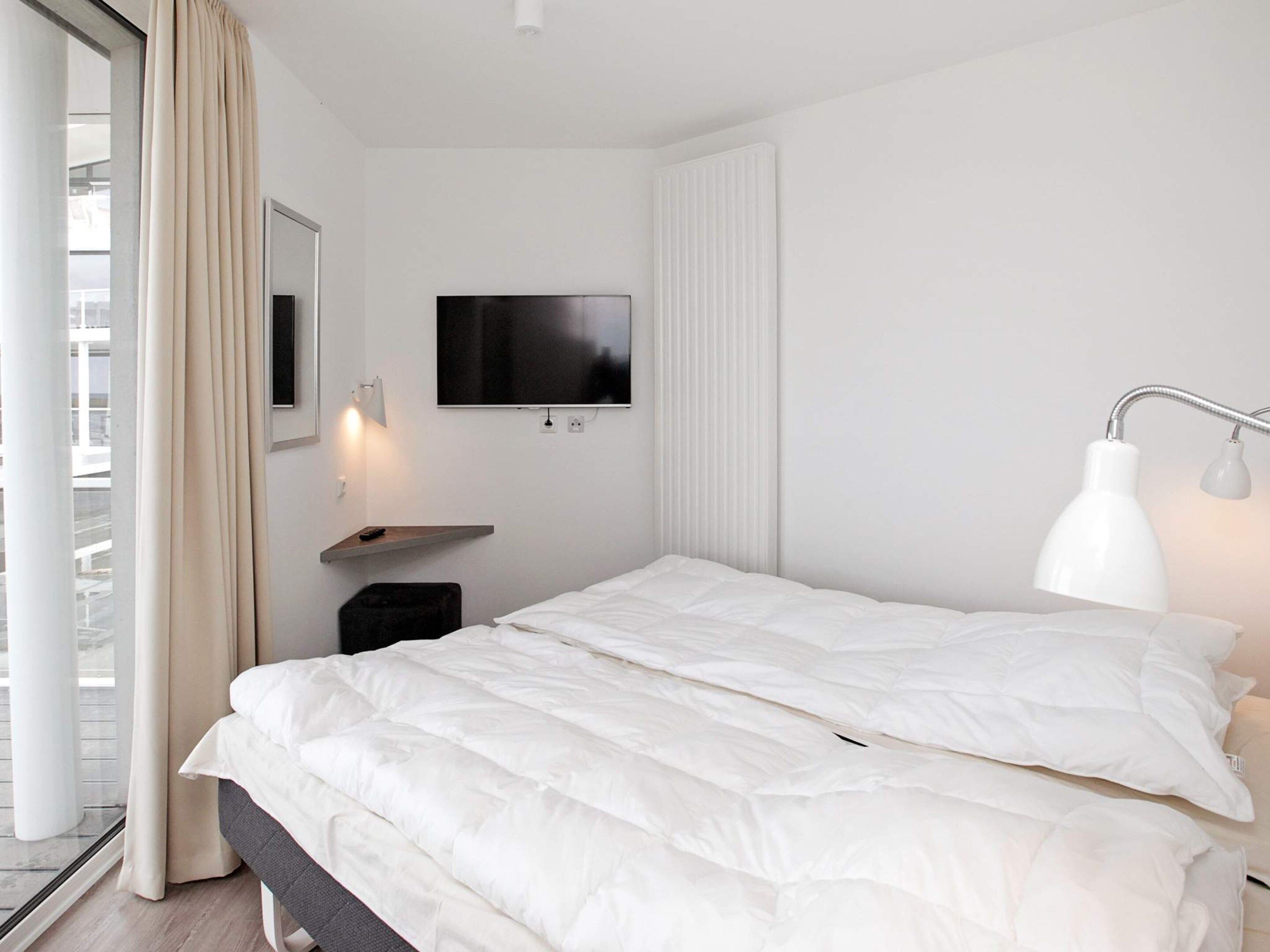 A modern hotel room with a bed, a television, a bedside lamp, and a window with curtains.