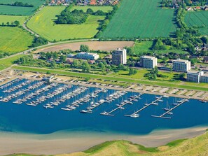 An aerial view of a marina with numerous boats docked, surrounded by green fields and residential buildings.
